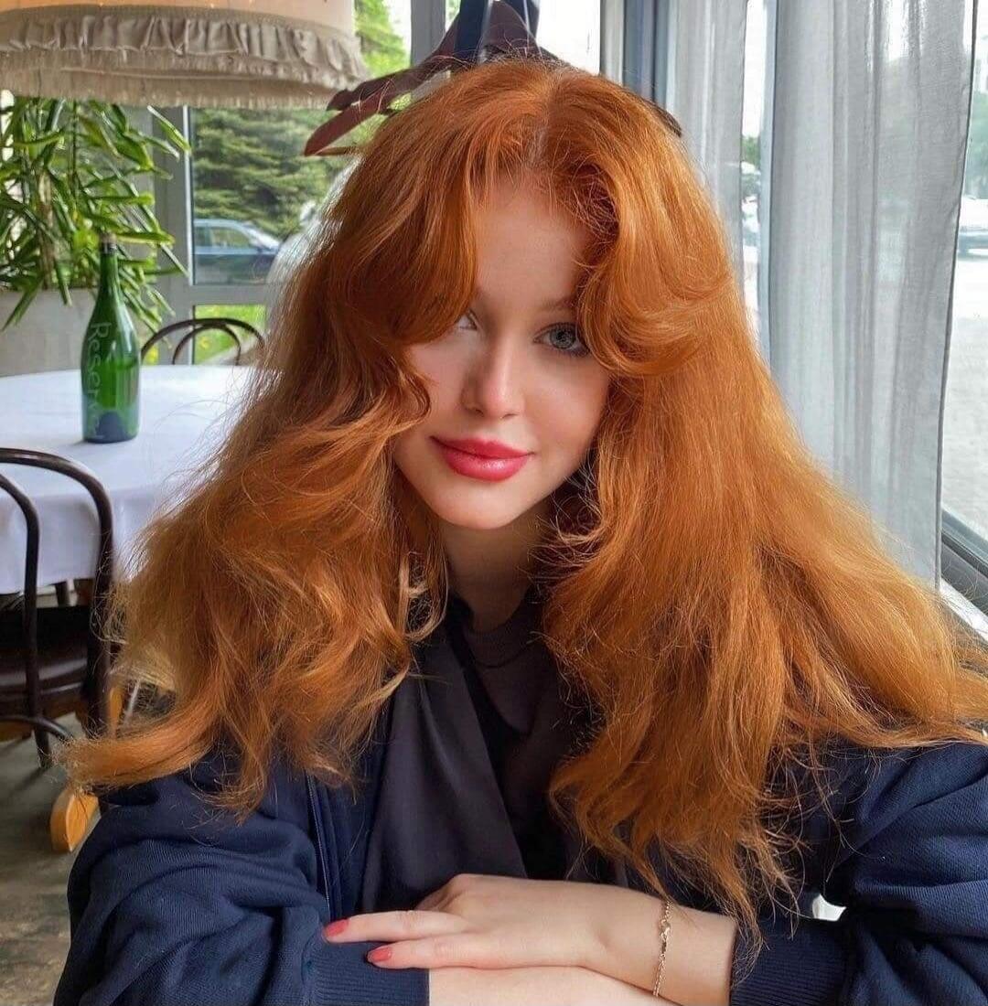 A woman with long red hair sits at a cafe.
