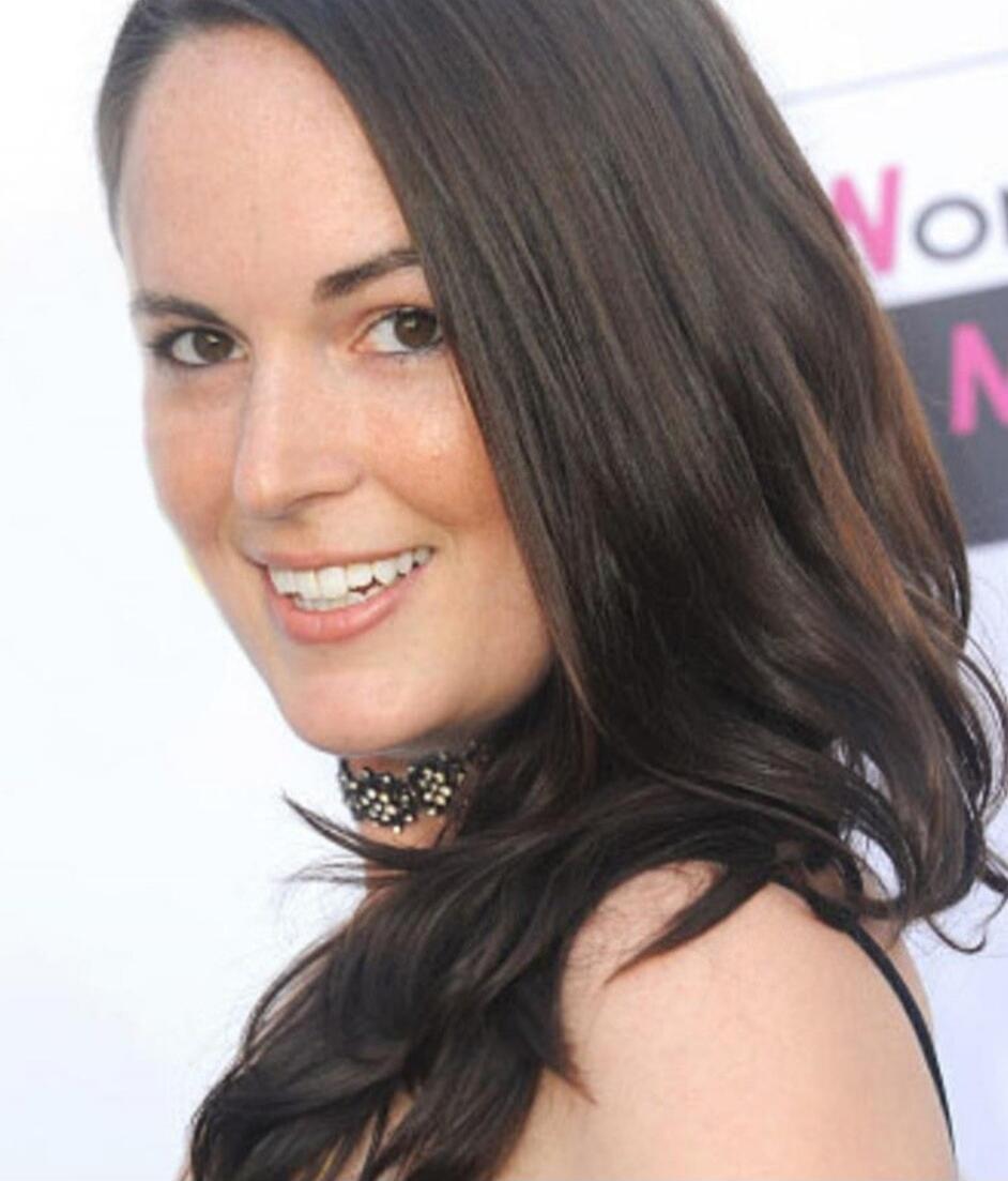 A smiling woman with long dark hair and a choker necklace. Partial text 'Wo N' is visible in the background.