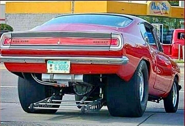 License plate reads 63082. A red classic car with oversized rear tires parked in a gas station lot.