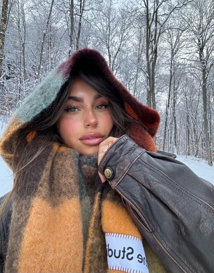 A woman wearing a colorful scarf and a leather jacket in a snowy forest.
