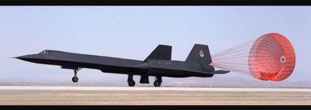 A black SR-71 Blackbird reconnaissance aircraft is landing on a runway, deploying a red drag parachute.