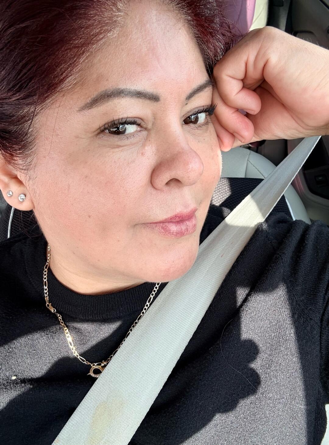 Woman in a car wearing a seatbelt, resting her head on her hand.