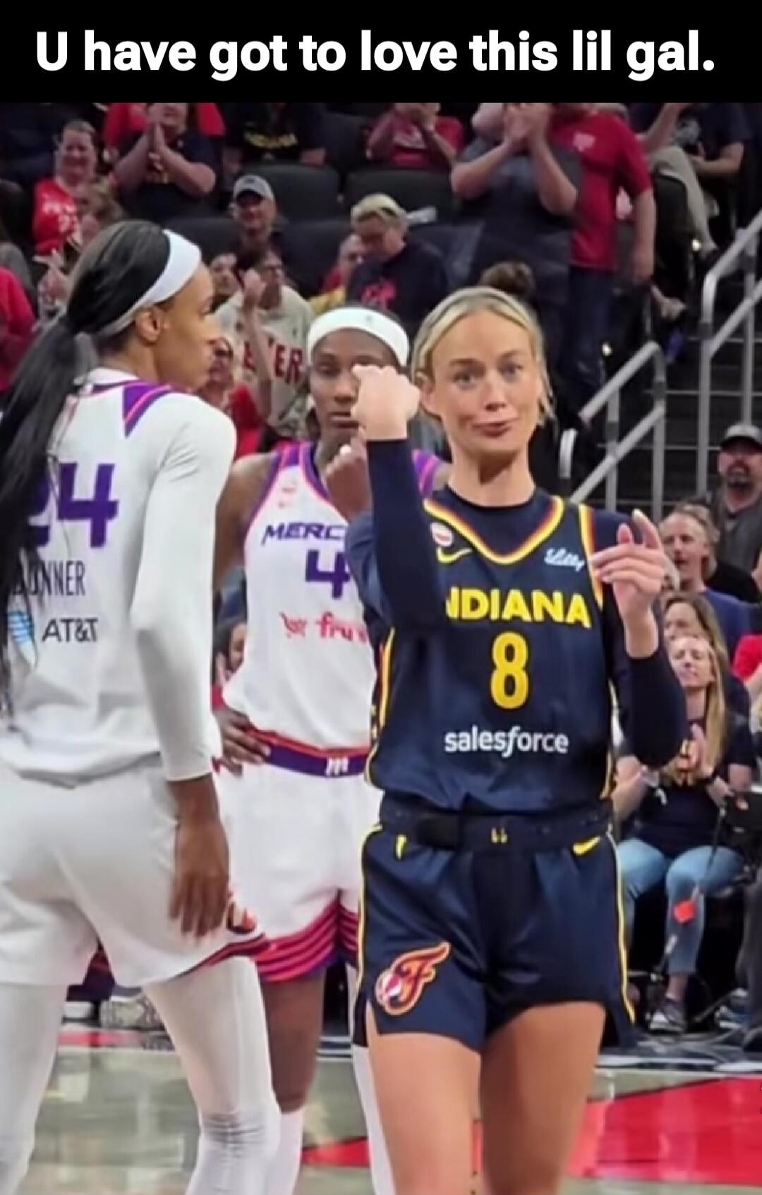 U have got to love this lil gal. A female basketball player in an Indiana uniform with number 8 makes a playful, sassy face and gesture, pointing from her eye to another player on the court, implying 'I'm watching you' or 'I see you'. Other players are visible in the background during a game.