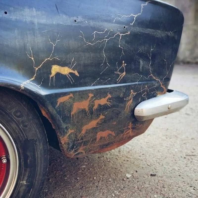 На автомобиле видны ржавчина и трещины по корпусу, а на боке нанесены силуэты скачущих лошадей в оранжево-рыжем оттенке.