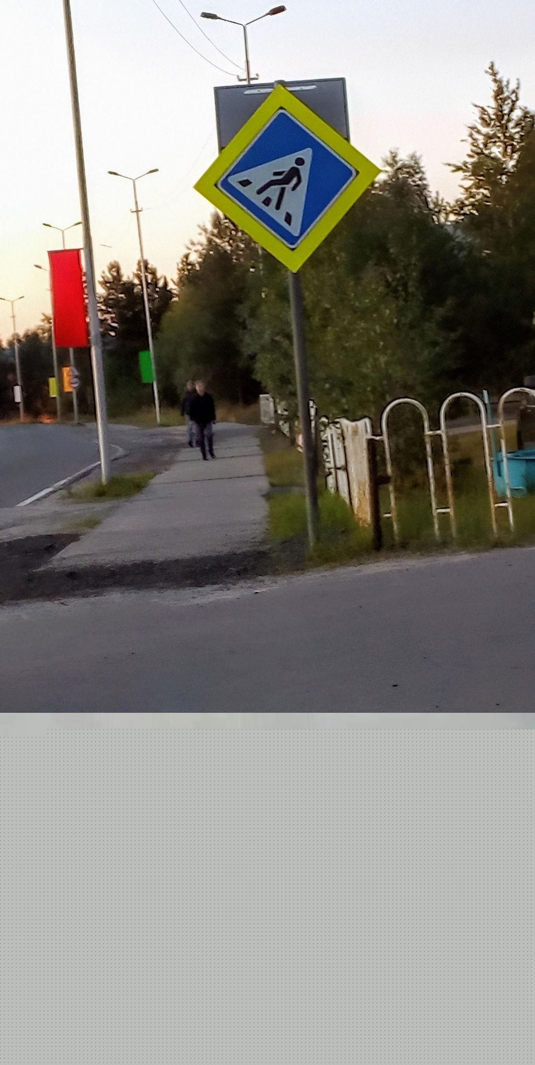 Уличный пешеходный переход. На заднем плане тротуар, люди идут по нему. Наклоненный квадратный пешеходный знак синий фон и желтая рамка надписью, обозначающий зону перехода.