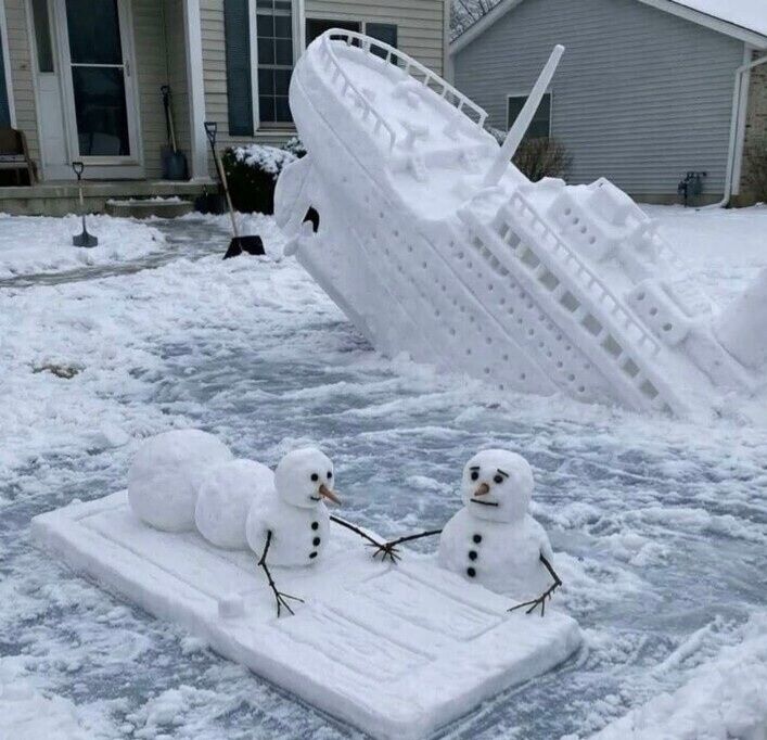 На фото виден перевернувшийся снежный корабль и две маленькие снеговички на снежной платформе; вокруг заснеженный двор дома.