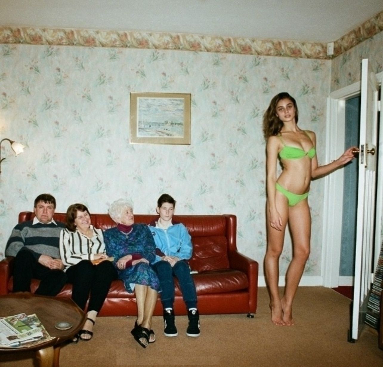 Фото семейное: молодая женщина в зелёном купальнике стоит у двери, на диване сидят четыре человека: три женщины и мужчина.