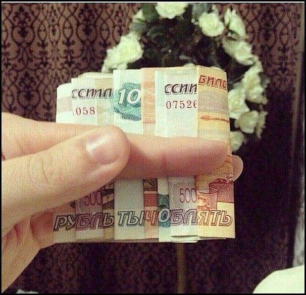 На фото рука держит сложенные банкноты (рубли) разного номинала, видны цифры: 10, 100, 500. Есть надпись на одной из купюр: «РУБЛЫ» (частично читается).