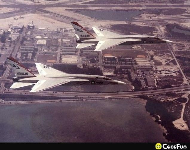 Two F-111 Aardvark jets flying in formation over a coastal area with an airport and urban development. Markings on the tails include 'GJ', '156625', and '156636'. A star insignia and '302' are visible on the fuselage. The image also contains a 'CocoFun' watermark.