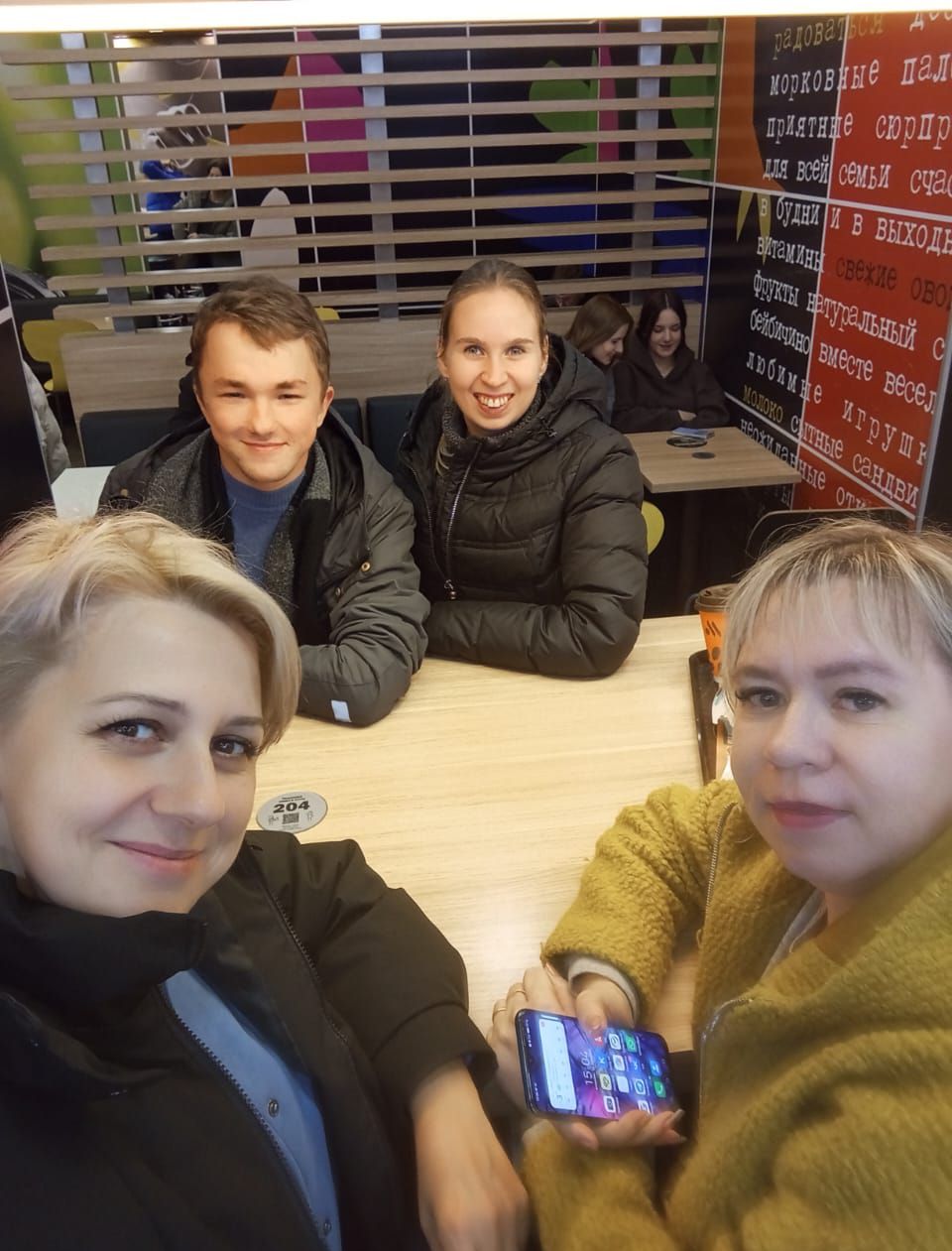 Группа людей сидит за столом в кафе, улыбаются.