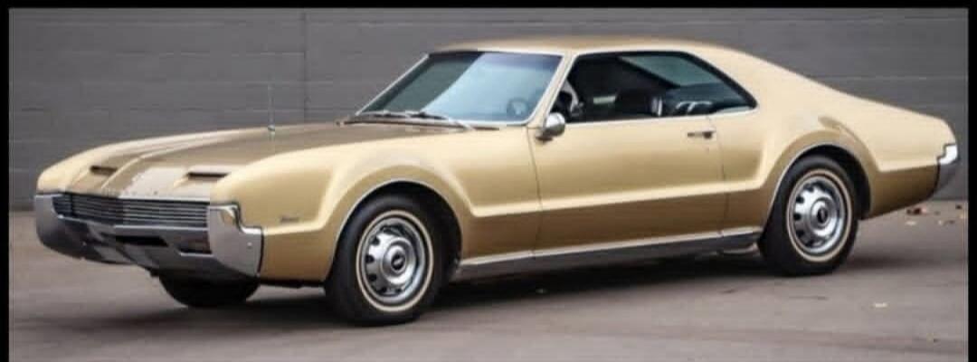 A vintage gold-colored car is parked on a paved surface.