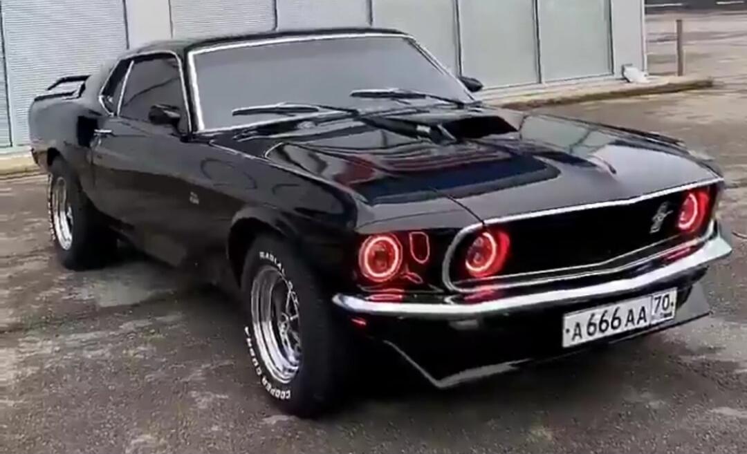 A black classic Ford Mustang with custom red halo headlights and a Russian license plate A666AA 70.