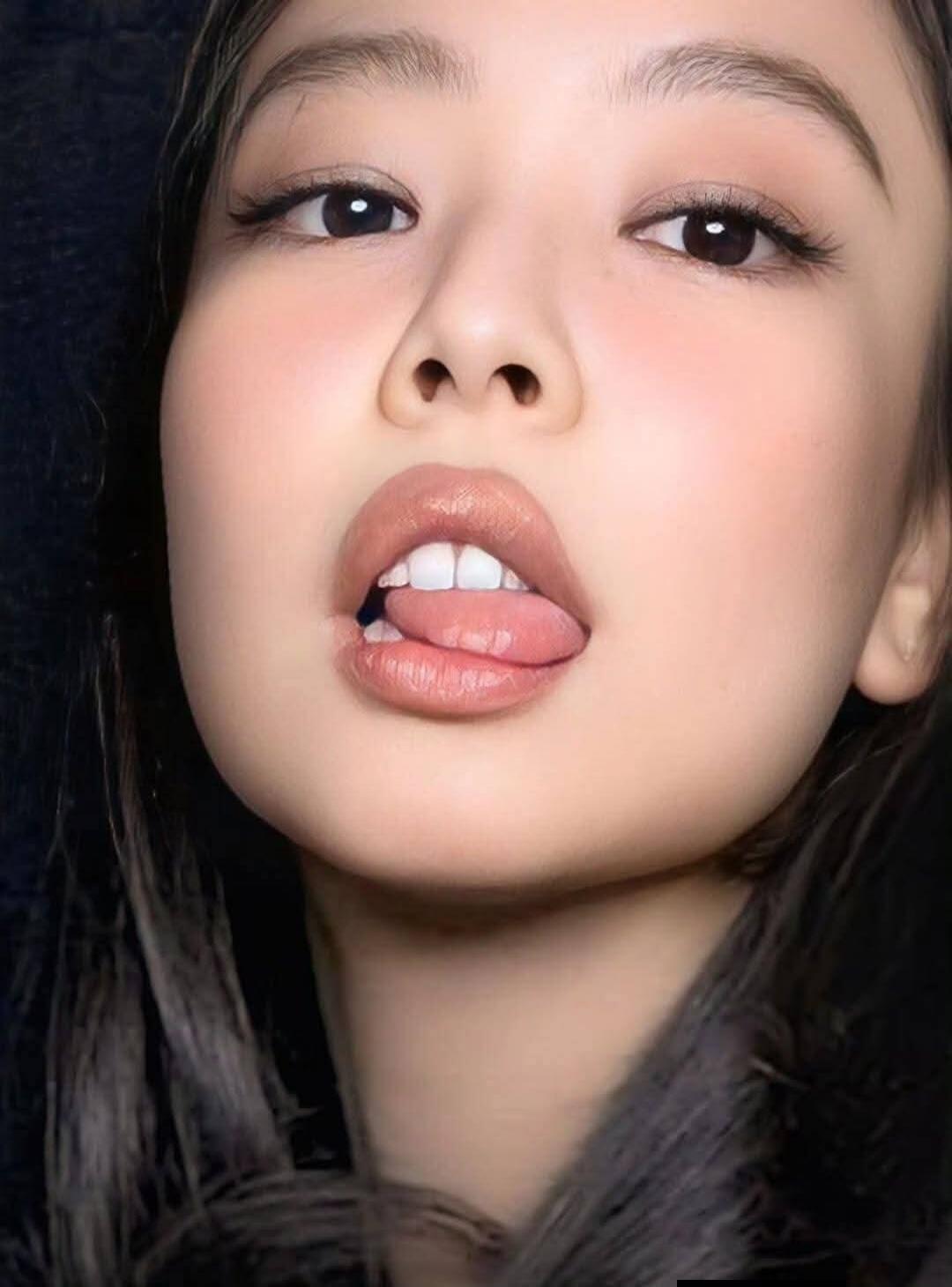 Close-up portrait of a young woman with glossy lips and subtle makeup, sticking her tongue out slightly.