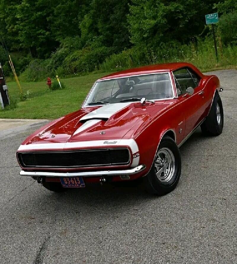 Red Chevrolet Camaro with white racing stripes, classic muscle car parked on a road.