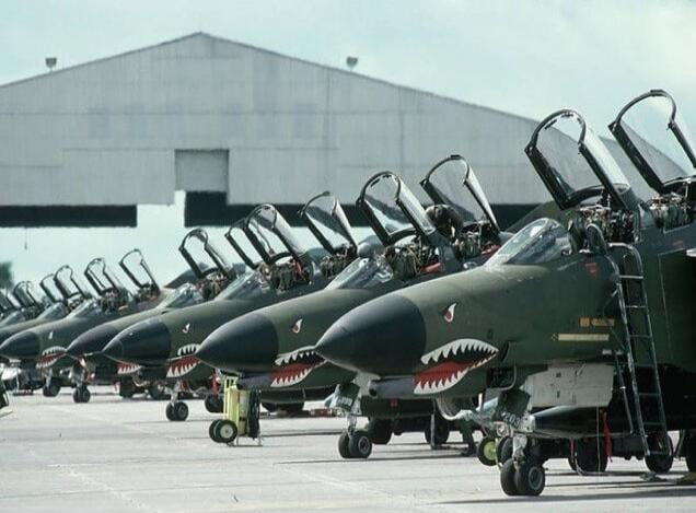Several fighter jets with shark-mouth noses lined up on a tarmac, their canopies open.