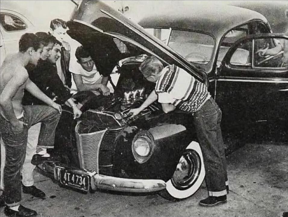 Group of men looking under the hood of a vintage car.