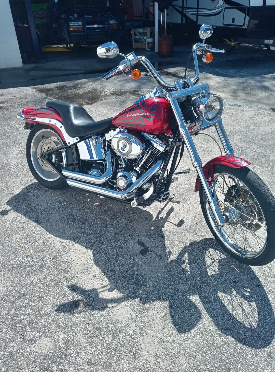 Red cruiser motorcycle with chrome exhaust and spoked front wheel; appears to be a Harley-Davidson-style motorcycle.