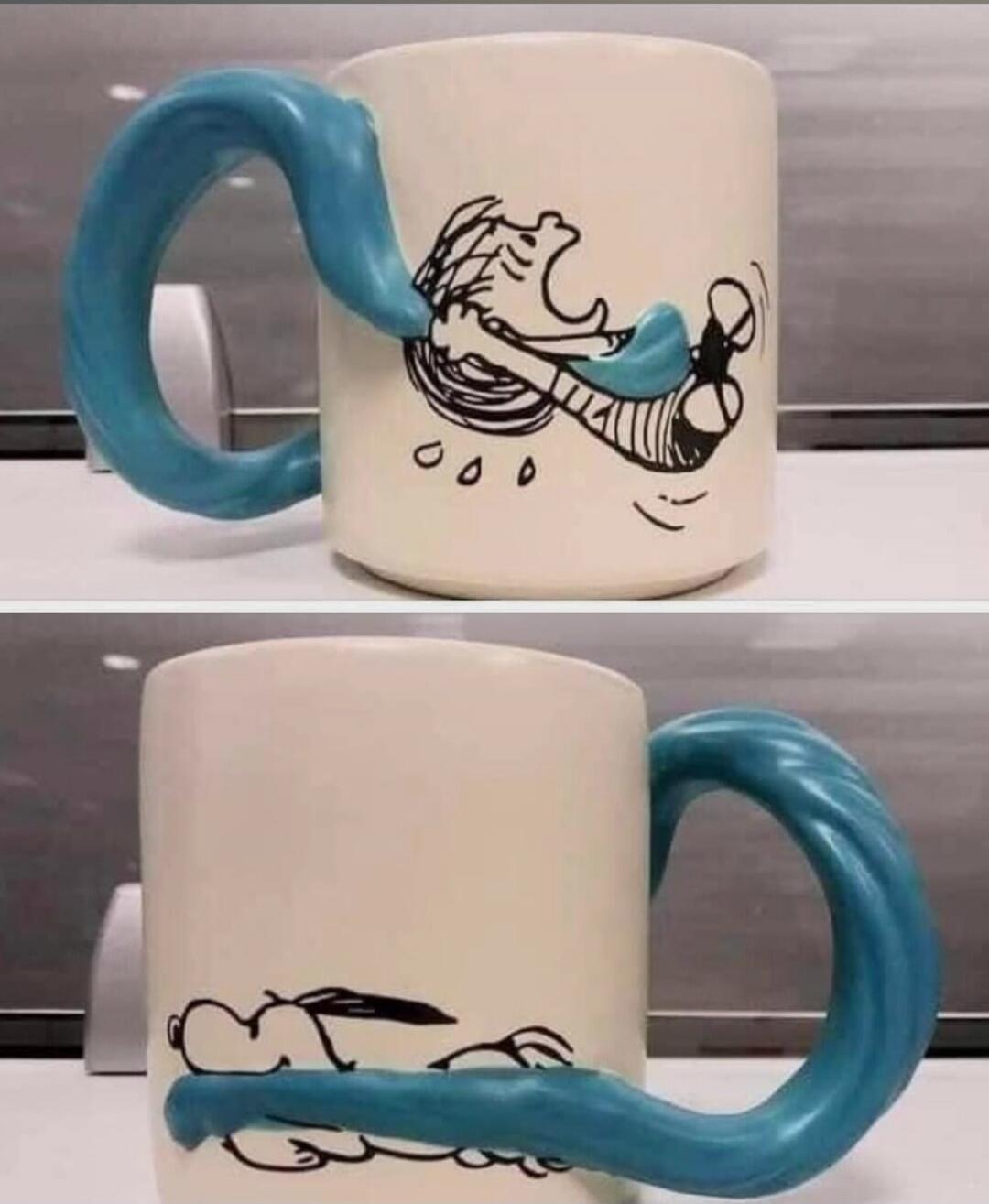A mug with a blue handle that humorously appears to grab a cartoon character.