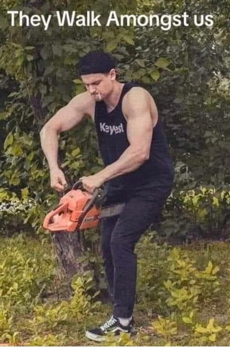 They Walk Amongst us. A muscular man in a black tank top and cap, with a cigarette in his mouth, is awkwardly holding a chainsaw, attempting to cut a tree trunk. He appears to be using the tool incorrectly.