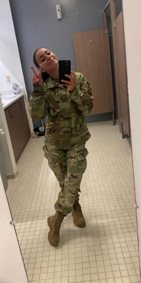 A person in camouflage military uniform taking a mirror selfie and making a peace sign.