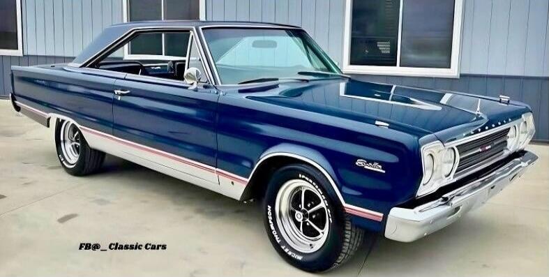 A dark blue classic car, a Plymouth Satellite, is parked outdoors. The car features chrome accents and white-lettered Mickey Thompson tires. A watermark 'FB@_Classic Cars' is visible in the bottom left corner.