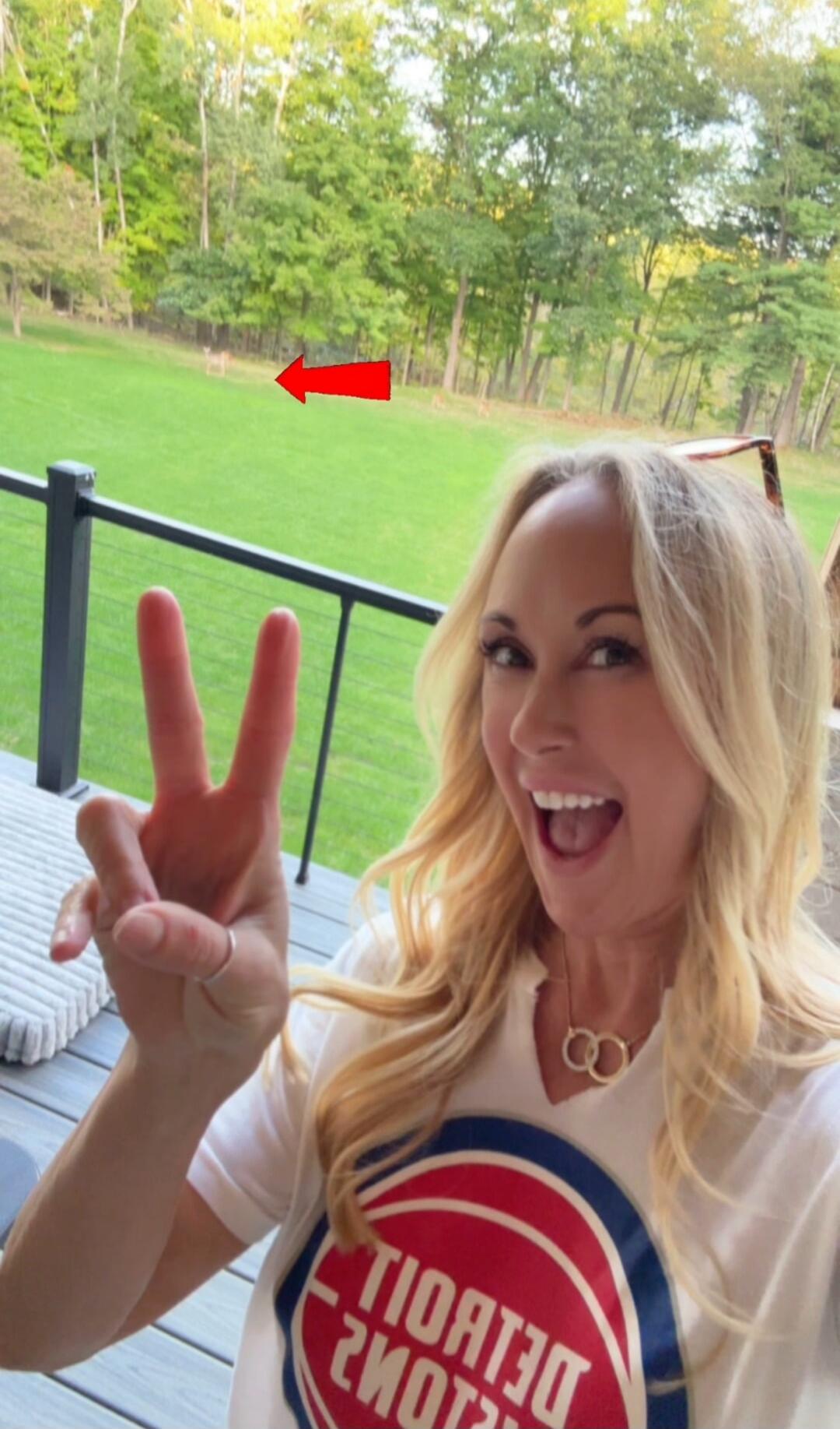 DETROIT PISTONS. A woman smiles and makes a peace sign, pointing to deer in the background.