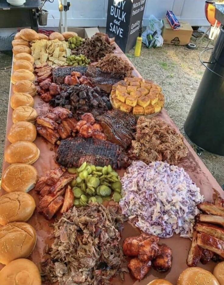 BUY BULK and SAVE Natural Beef Pasture Fed Quality Assured. A large spread of barbecue food including pulled pork, brisket, ribs, chicken, buns, pickles, coleslaw, and cornbread.