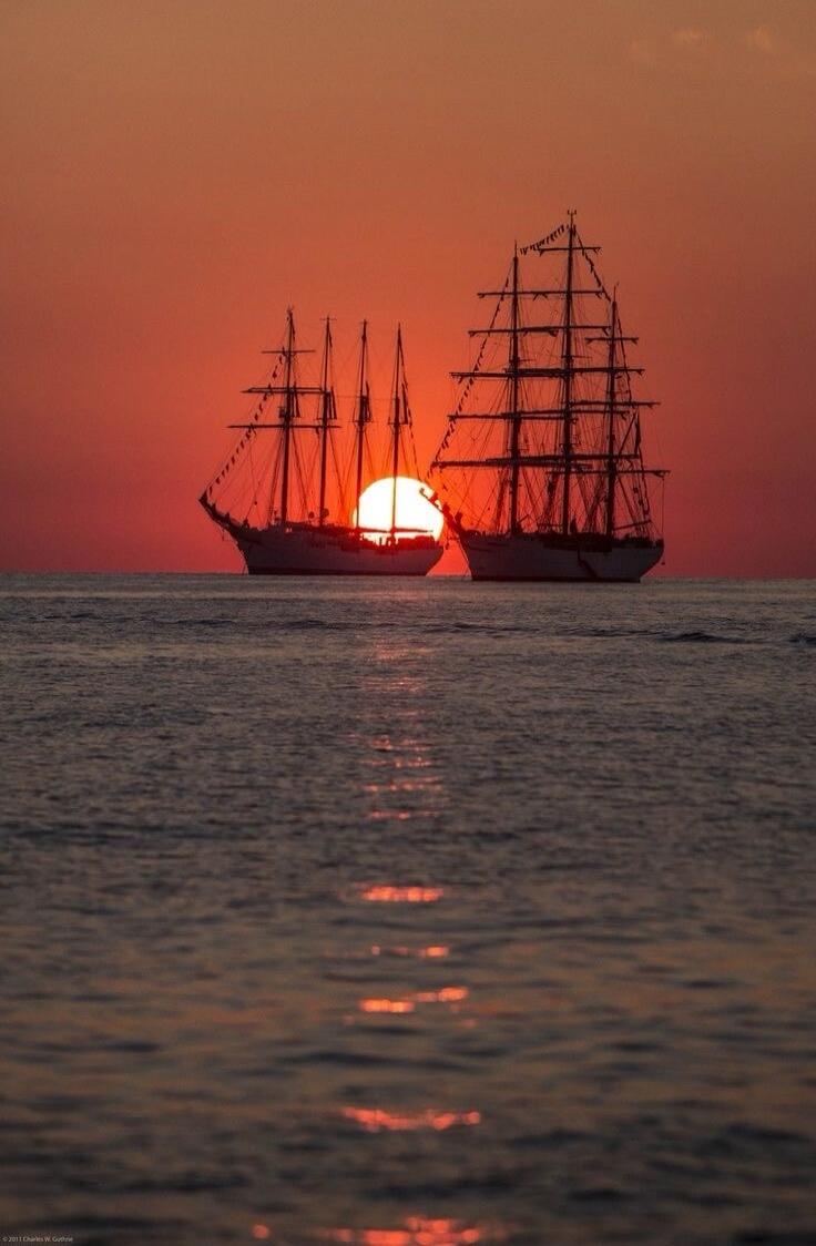 Two sailing ships silhouetted against a vibrant sunset.