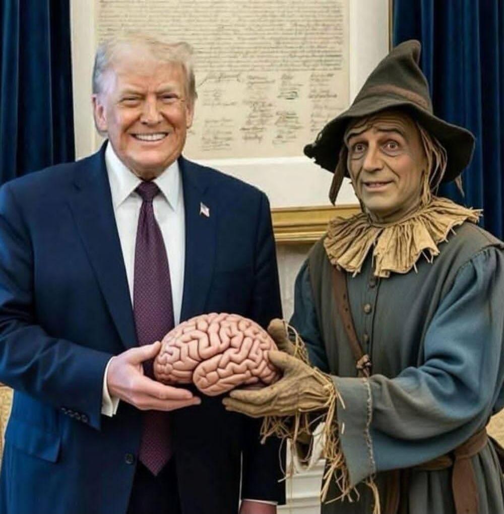 Donald Trump holding a prop brain while standing next to a person dressed as a scarecrow.