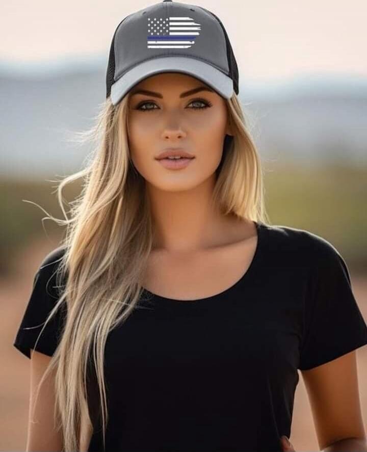 A woman wearing a grey baseball cap with a Thin Blue Line American flag design and a black t-shirt.