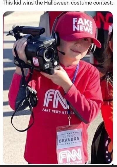 This kid wins the Halloween costume contest. FAKE NEWS NETWORK on shirt. Hat says FAKE NEWS. Badge reads LET'S GO BRANDON. FN logo on shirt.