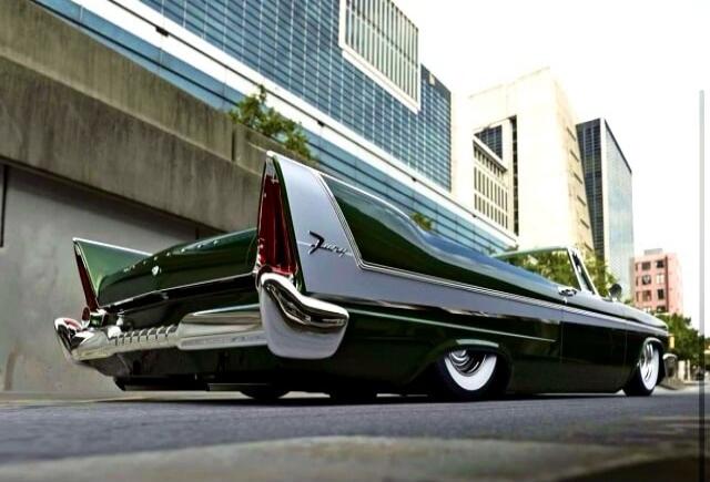 A black vintage lowrider car with large chrome fins parked on a city street.