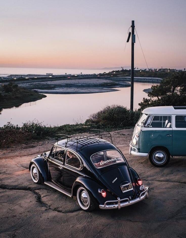 Beetle and a vintage van parked near the coast at sunset.