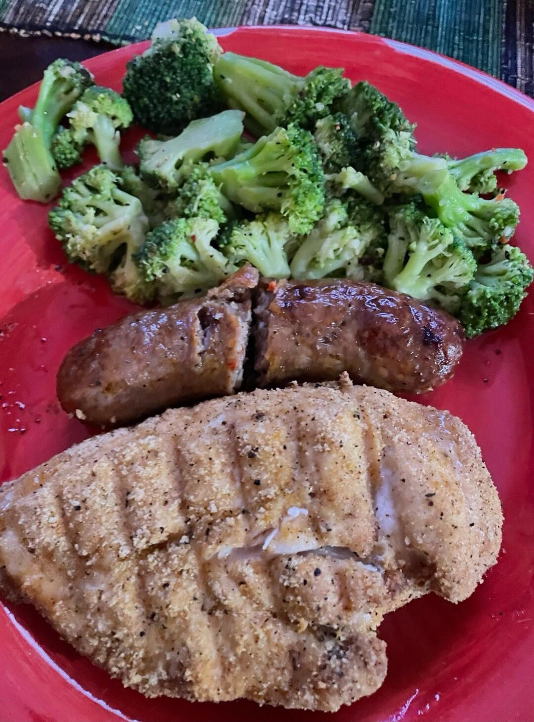 Breaded chicken breast with broccoli florets on a red plate. Session ID: 1001264.