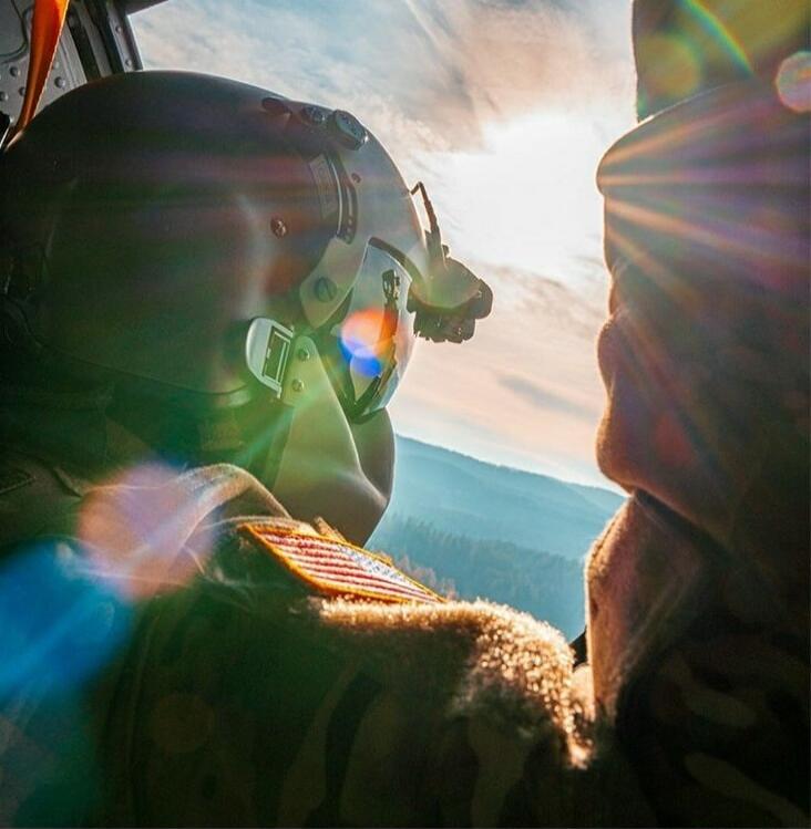 Photograph of a person wearing a flight helmet and headset, looking out of an aircraft cockpit with sun glare and lens flares.