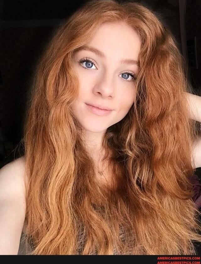 Portrait of a young woman with long wavy red hair, blue eyes, looking at the camera.