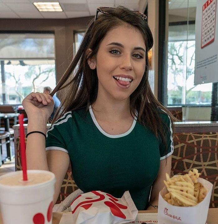 A young woman sitting in a fast-food restaurant with fries and a drink.