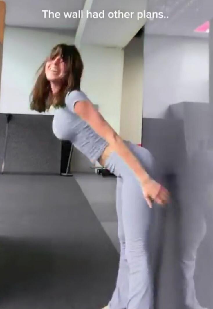 The wall had other plans.. A woman in a gym attempts a dance move or twerk, but bumps into the wall, reacting with a laugh or grimace.