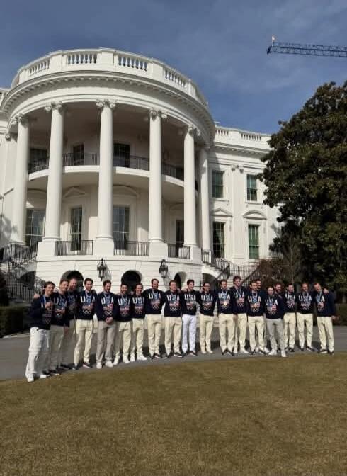 A group of men in athletic wear stand in front of the White House.