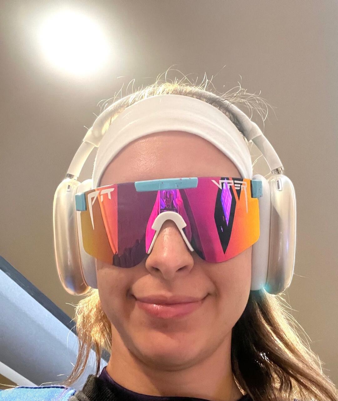 Person wearing colorful oversized VR goggles and large over-ear headphones, smiling at the camera.
