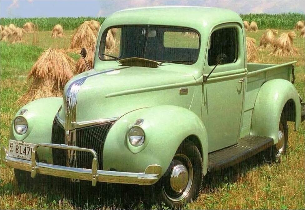 A vintage green pickup truck in a field with haystacks. License plate reads R 8147.