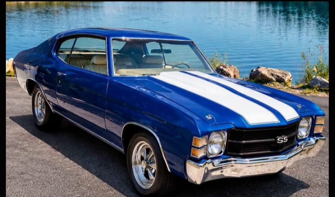 A classic blue Chevrolet Chevelle SS with white racing stripes is parked by a lake. The 'SS' logo is visible on the front grille.