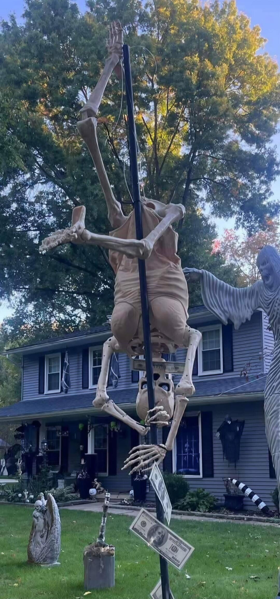 A Halloween yard decoration featuring a skeleton hanging from a pole with fake dollar bills.