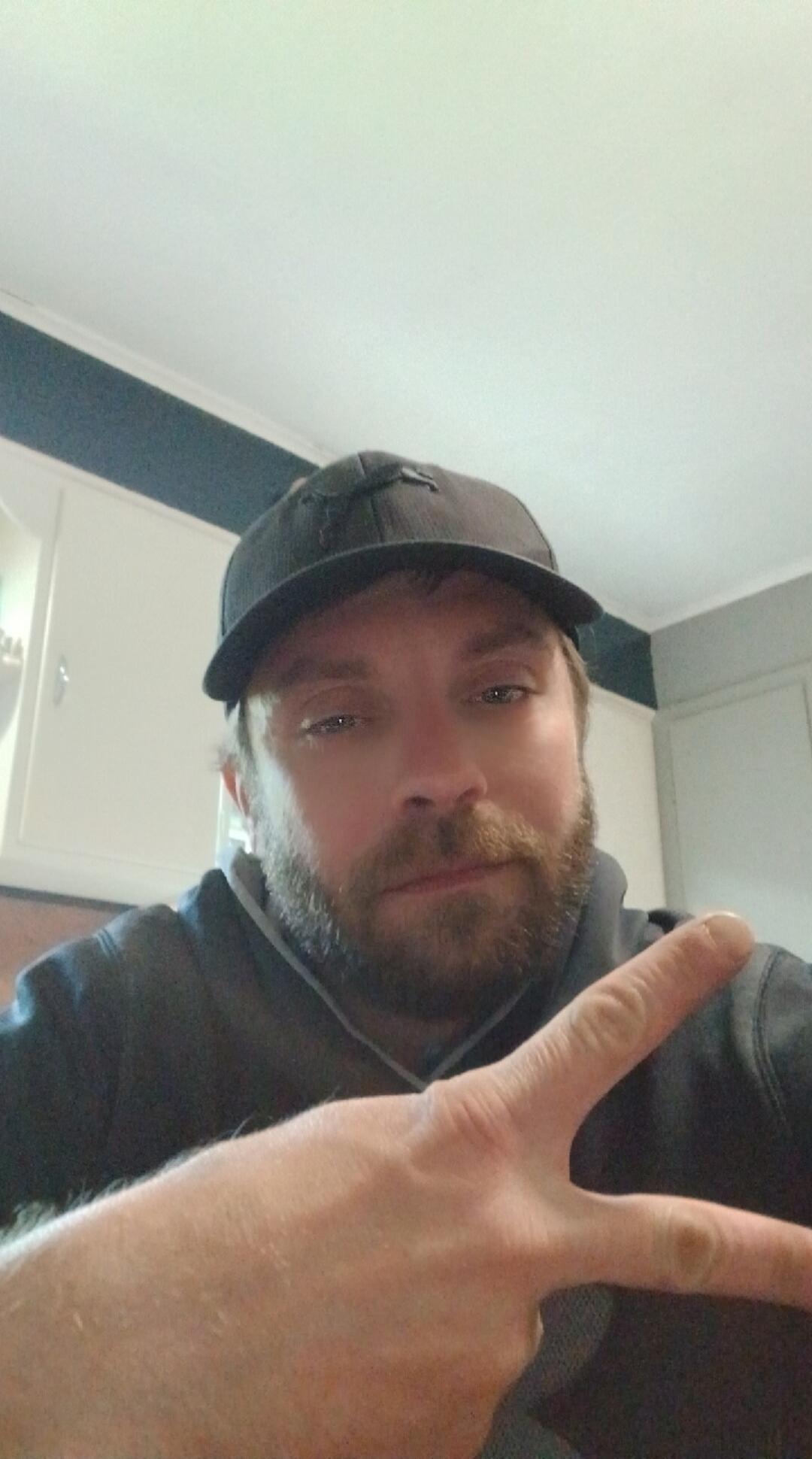 A man with a beard and a baseball cap is making a peace sign with his hand.