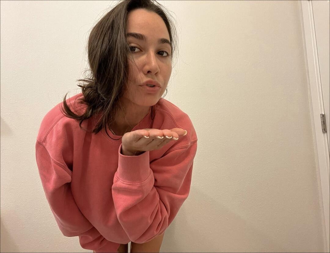 A woman in a pink sweatshirt blowing a kiss.