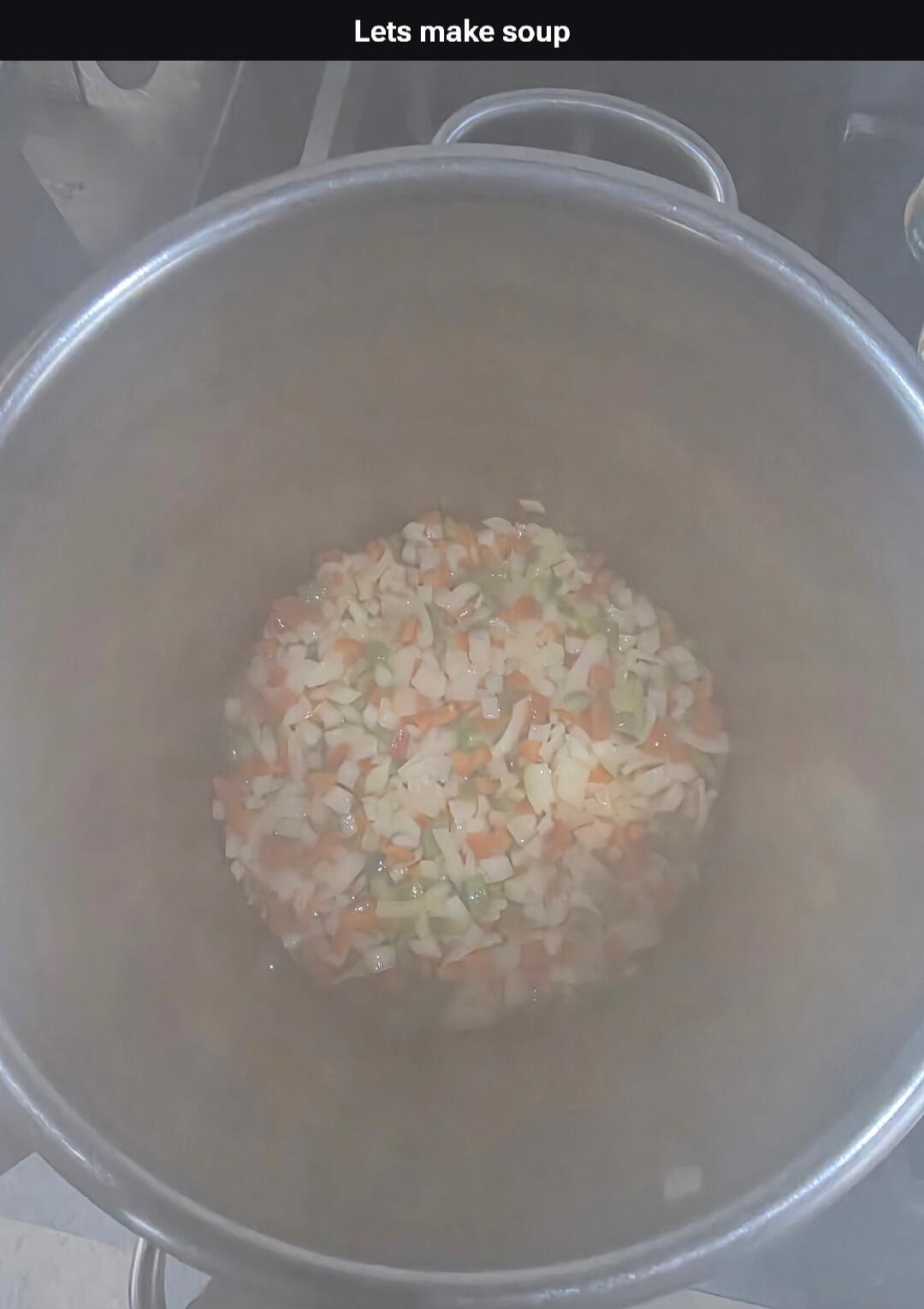 Lets make soup. A large pot filled with chopped vegetables, including carrots, celery, and onions, steaming as they cook.