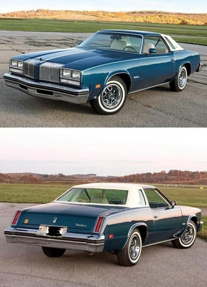A classic blue Oldsmobile Cutlass Supreme car is shown from the front and rear angles, parked on an asphalt surface with a grassy field and trees in the background.