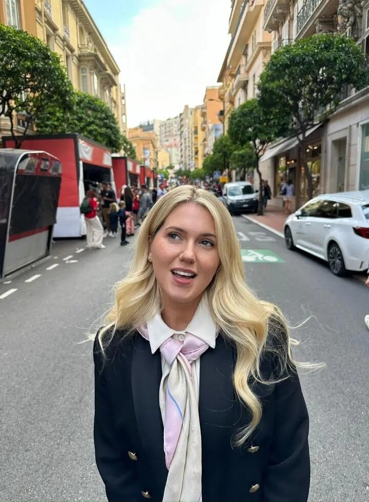 A young woman standing on a city street with buildings and pedestrians in the background.