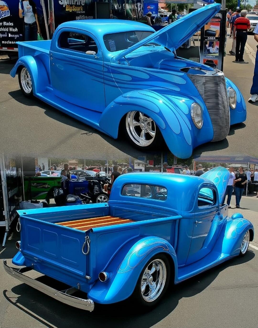 Spitfire BigSpark, spitfire.com, clean, blades, wash, mucus. A custom blue hot rod pickup truck with flame graphics, chrome wheels, and a wooden bed. The hood is open, revealing the engine bay. People are visible in the background at what appears to be a car show or event.
