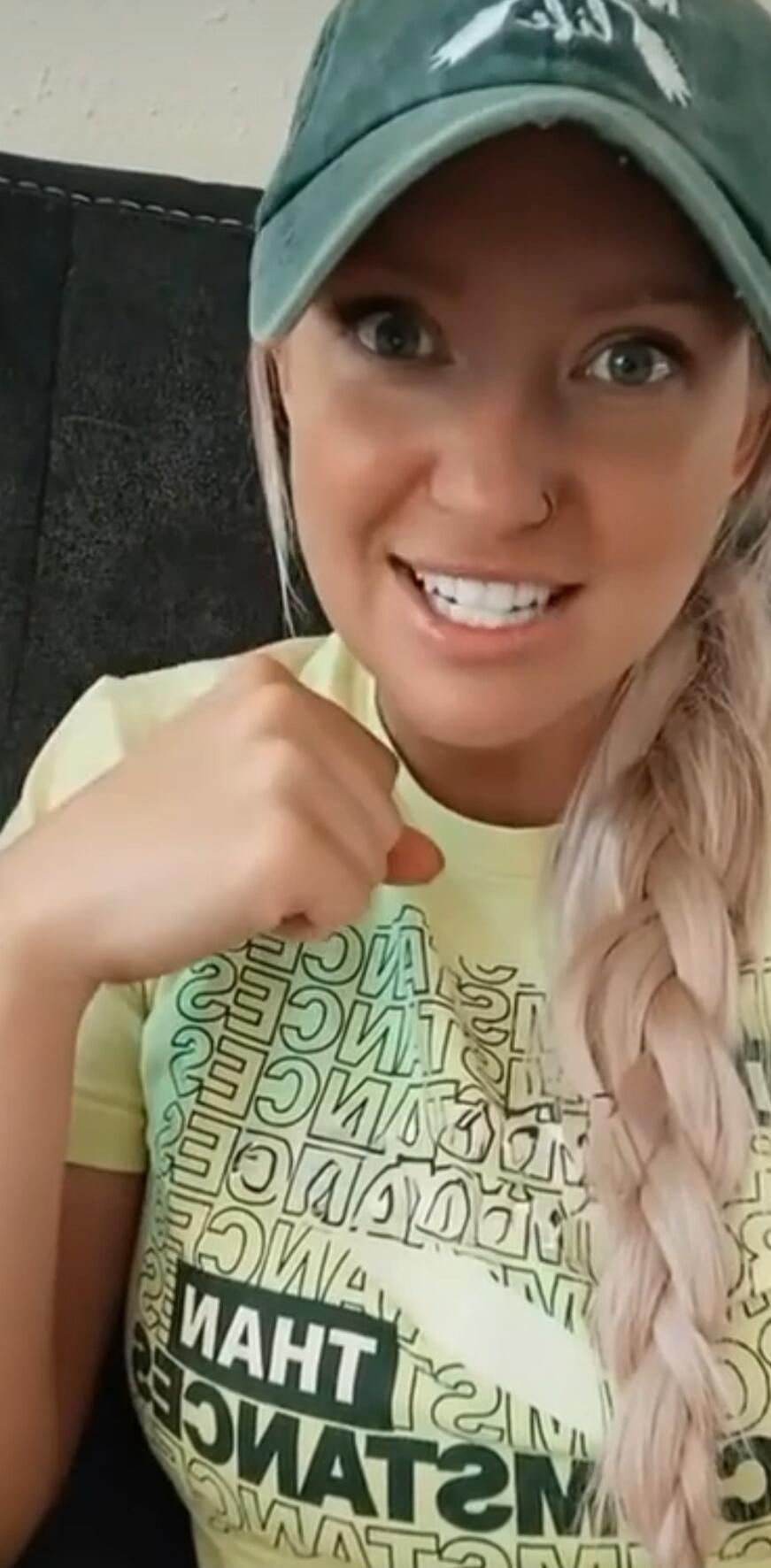 Photo of a smiling woman wearing a green cap and a light-colored shirt, with a long braided hair.